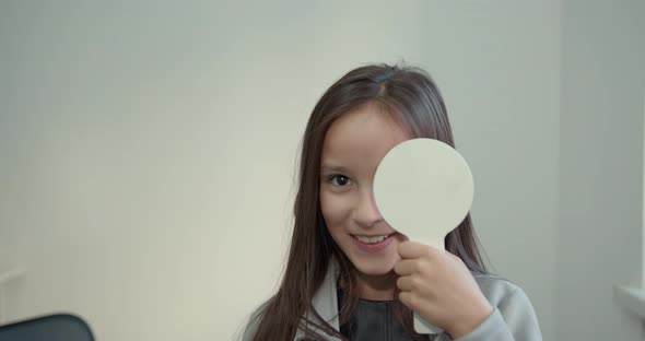 Schoolgirl Girl with a White Sign Closes Her Eye in the Ophthalmologist's Office