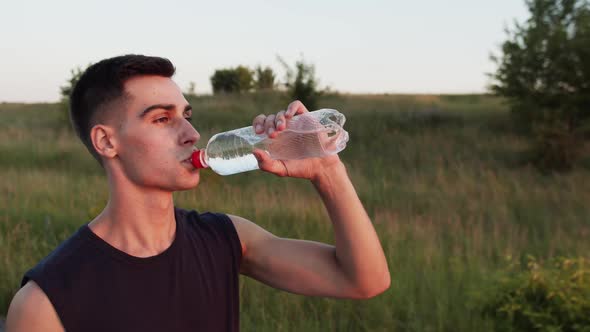 Handsome Sportsman Drinking Water From a Bottle and Smiling at Camera Outdoor