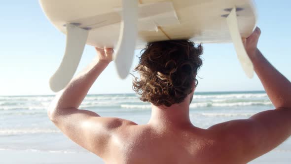 Man carrying surfboard on head at beach on a sunny day