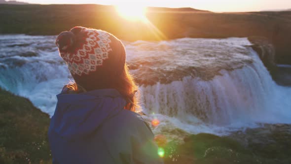 Rear View of Young Woman in Hat Looking at Waterfall During Sunset Slow Motion