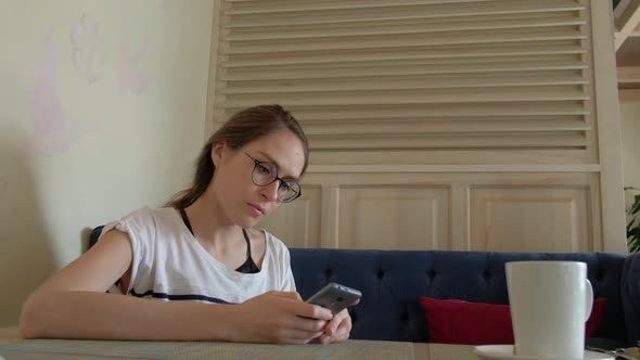 Cute Female Using Smartphone and Drinking Coffee in the Cafe