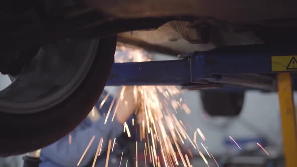 Male Unrecognizable Caucasian Auto Mechanic Welding Car. Professional Working in Repair Shop