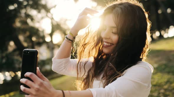 Young pretty woman taking selfie with smartphone in a green park