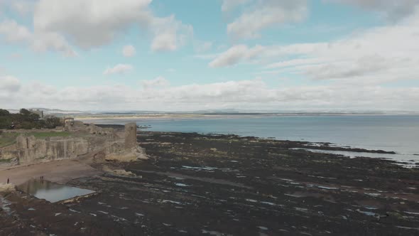 Aerial drone view of St Andrews Castle in Scotland, UK. Slowly flying over rocky coastline approachi