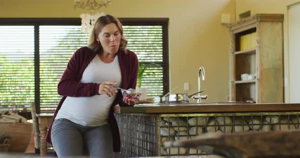 Caucasian pregnant woman sitting in kitchen and eating ice cream