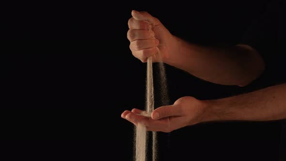 Stream of Dry Sand Pours Into Palm of Man and is Spilling Through His Fingers on Black Background