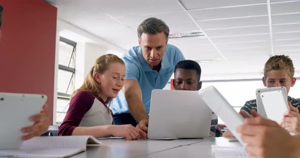 Teacher assisting schoolkids on laptop 4k