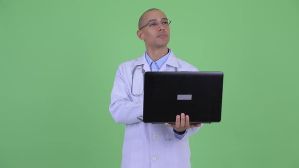 Happy Bald Multi Ethnic Man Doctor Thinking While Using Laptop