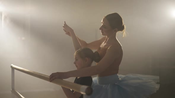 Side View Medium Shot of Slim Ballet Teacher in Blue Tutu Teaching Fourth Hand Position to Student