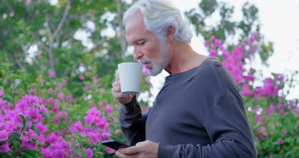 Senior man having coffee while using mobile phone 4k