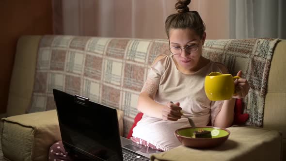 Young pregnant woman watching tv series and eating cake with tea at home