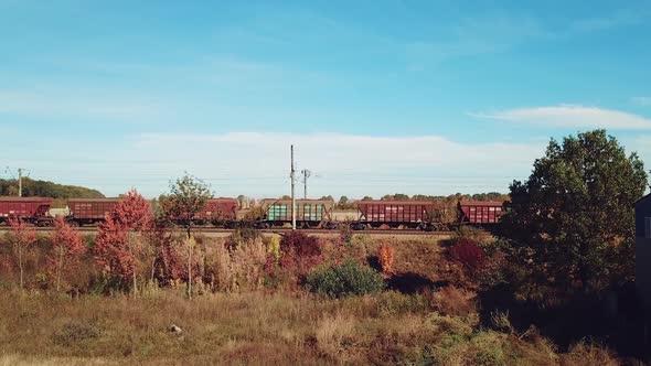 carriages of freight train are passing by rail in the field on the background of buildings