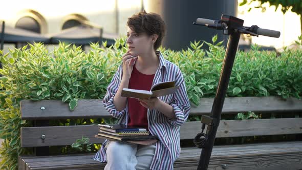 Front View Portrait of Slim Beautiful Young Woman Reading Book Outdoors Looking Away Dreaming