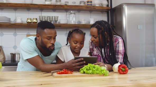 Happy Black Family Reading Vegetarian Recipe on Tablet Pc Cooking Together in Kitchen