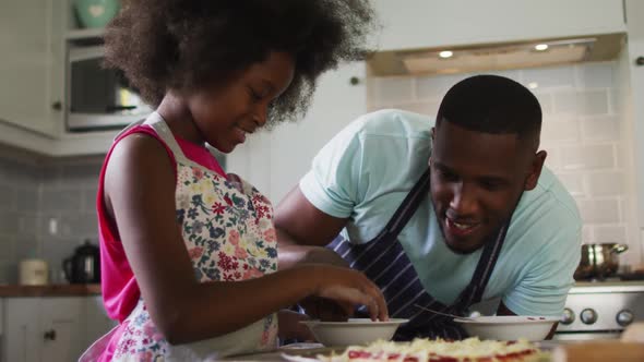 African american daughter and her father making pizza together in kitchen