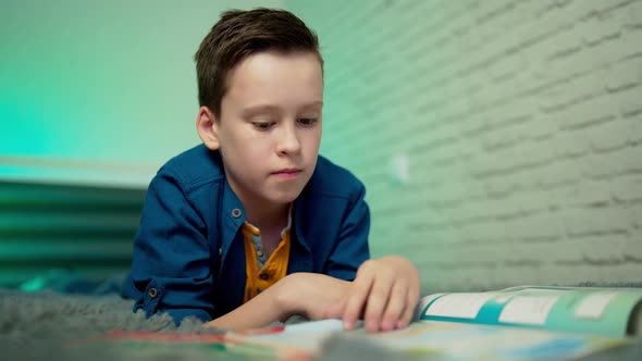 Little boy lying on bed reading book at home. Home education.