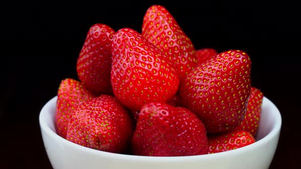 Strawberries without tails lie in white bowl or plate. It rotates