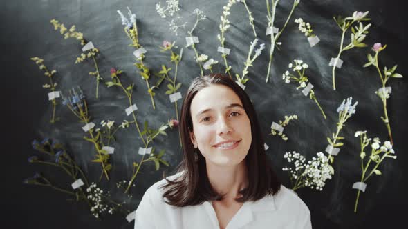 Young Cheerful Woman Posing against Wall Decorated with Wildflowers