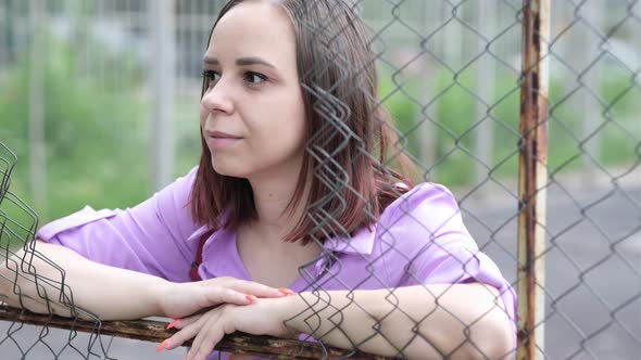 Young Woman with Short Hair in Purple Shirt Looking Away Through Hole of Lattice Fence