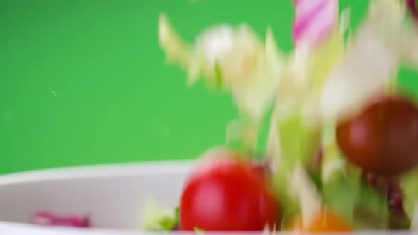 Fresh salad falling into bowl on green background