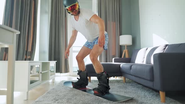 Fun Video. Man in Shorts and a T-shirt Depicts Snowboarding on a Carpet in a Cozy Room. Waiting for