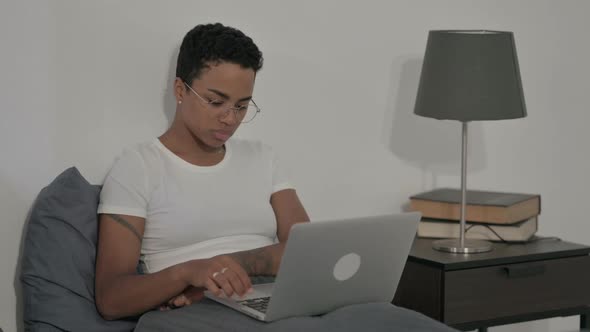 African Woman Thinking While Working on Laptop in Bed