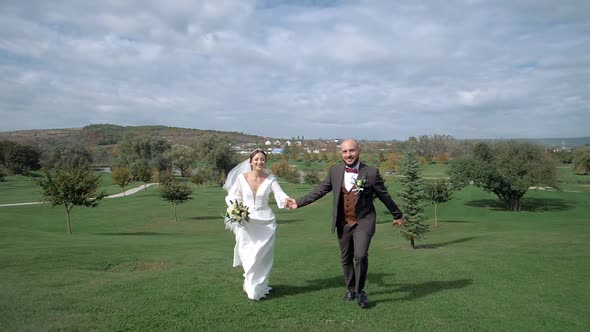 An engaged man and girl run holding hands on a huge, beautiful golf course