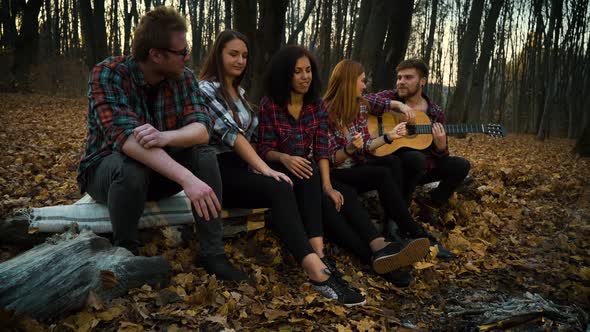 Happy Hikers Relaxing By Campfire and Listening To Guitar