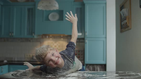 Blonde preschooler having fun with flour on blue kitchen