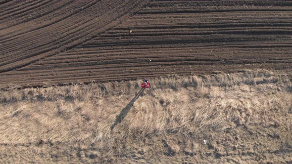 Aerial View of Woman Farmer with Digital Tablet Computer Looks at a Fresh Plowed Field After Winter