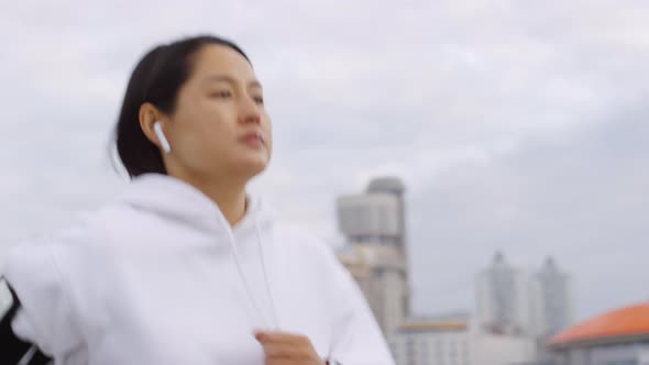 Asian Woman in Wireless Earphones Jogging along City Riverside