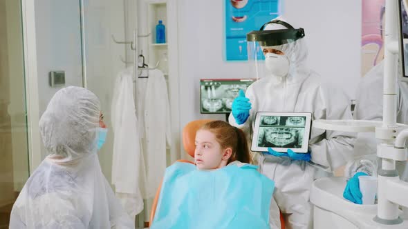 Dentist with Face Shield Explaining Panoramic Mouth Xray Image to Mother of Kid
