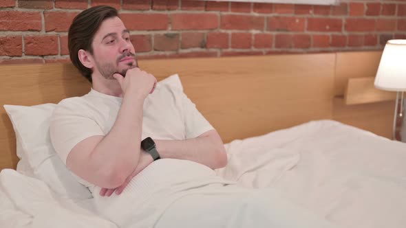 Casual Young Man Thinking While Sitting in Bed