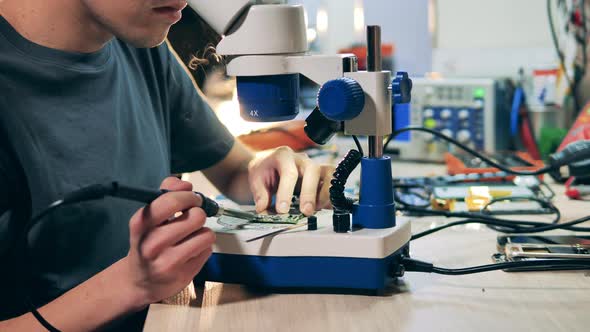 Repairman is Using a Microscope While Fixing a Circuit