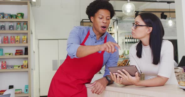 Video of happy diverse female owner and male waiter working with tabletat cafe shop