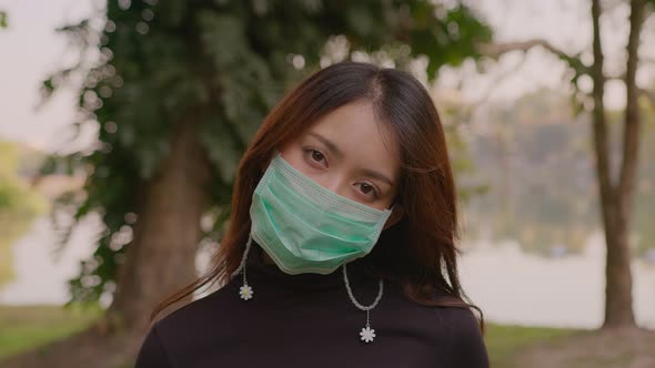 Portrait of Happy Thai Young Woman Wearing Protective Face Medical Mask Standing in Park at Sunset