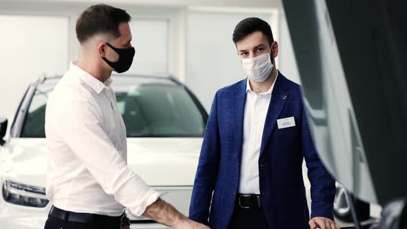 Agent Showing Car Engine Under Open Hood to a Client in Auto Showroom During Lockdown