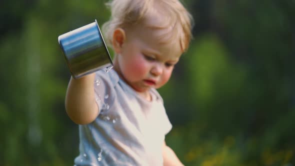 one year old baby spills liquid from a metal mug. The concept of walking outdoors,