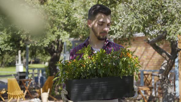 Portrait of Cute Bearded Farmer Holding a Pot of Flowers in Hands Looking at Camera Smiling Standing