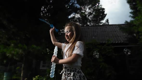 Little Girl Plays with Soap Bubbles Outdoors