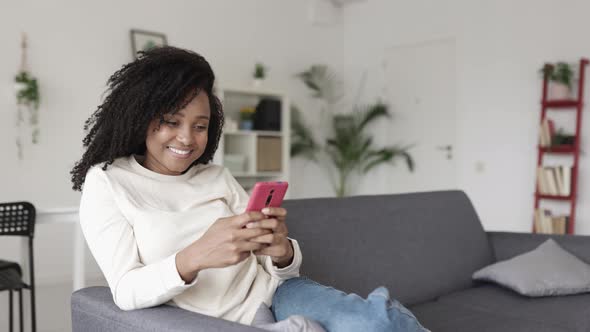 Happy Young Woman Using Mobile Phone Relaxing on Sofa at Home