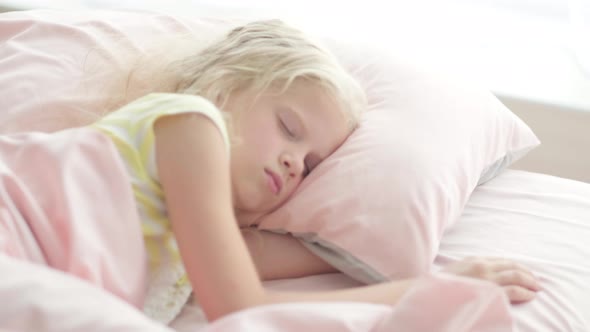 Adorable Blonde Girl Sleeping Sweetly in the Morning on Pink Bed Linens at Home