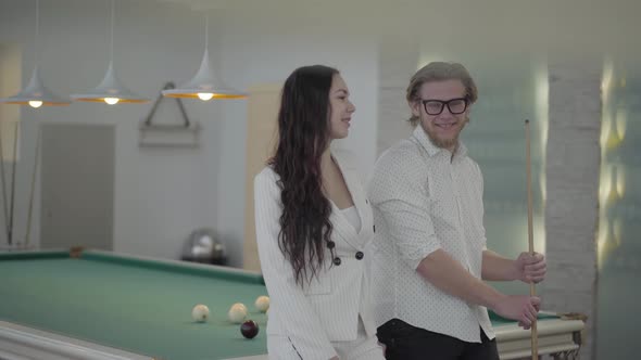 Blond Bearded Man and His Girlfriend Talking Near the Billiard Table. Confident Man in White Shirt