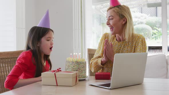 Girl blowing cake while having a video chat on laptop at home