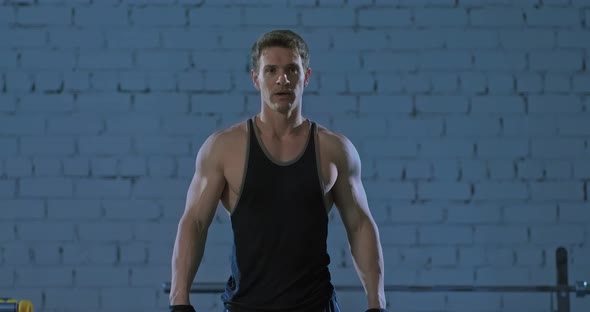 Muscular Male Athlete Stands and Breathes Deeply After Exercise in the Gym