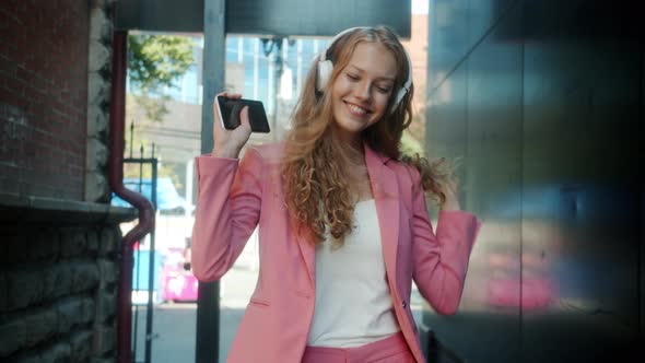 Portrait of Happy Young Lady Enjoying Music Through Headphones Walking Holding Smartphone in City