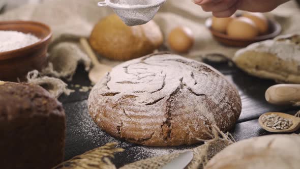 In the Bakery, a Baker After Baking Fresh Bread Sprinkles Sugar Powder (Flour) on Bread (Flour