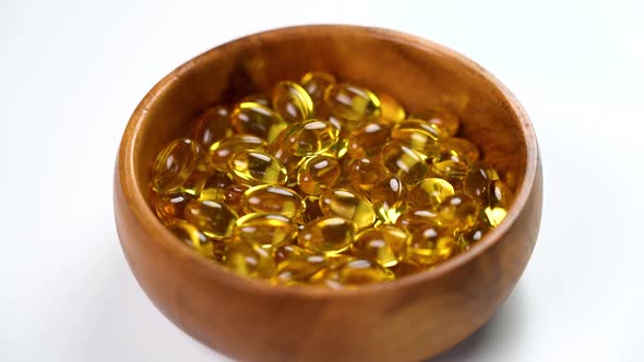 Yellow softgel omega 3 capsules. Fish oil pills falling into a wooden eco bowl in slow motion