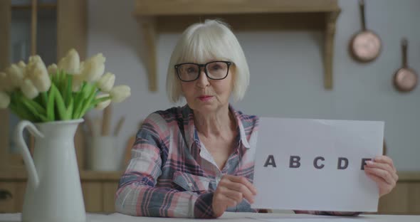 Senior Teacher in Glasses Showing Sheet of Paper with Alphabet Letters Looking at Camera. Online