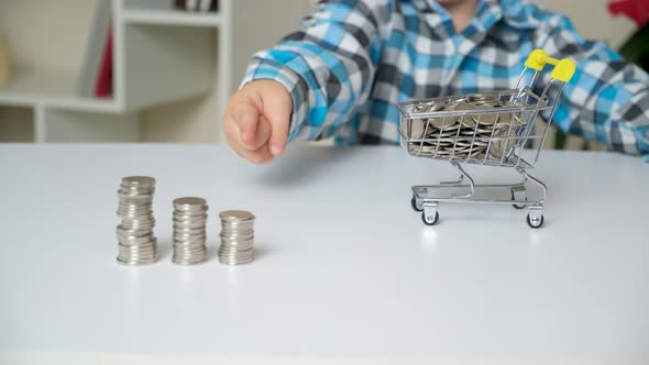 The Boy Puts the Coins in a Cart and Points His Finger at the Towers of Coins